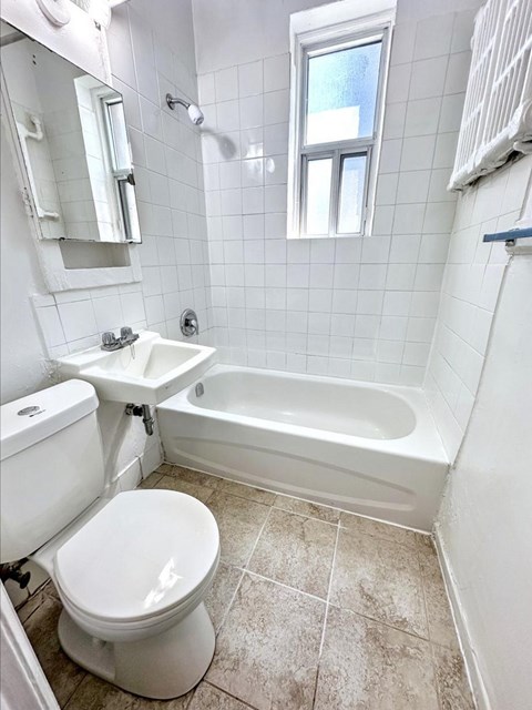 A white toilet sits in a small bathroom with a white tub and sink.