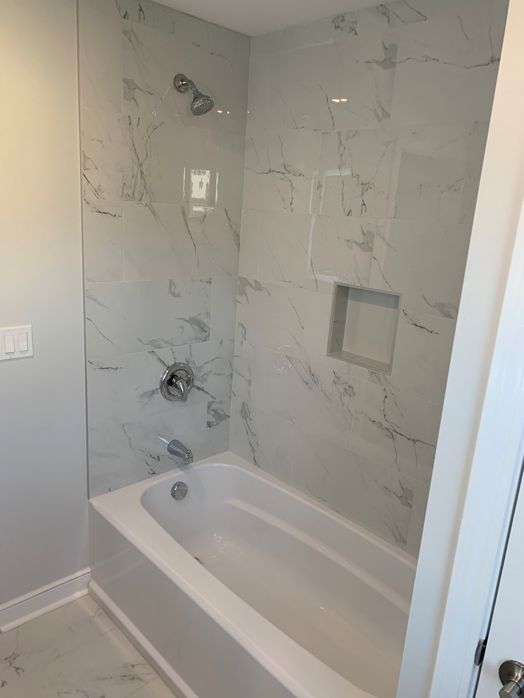 A white bathtub with a marble wall behind it.