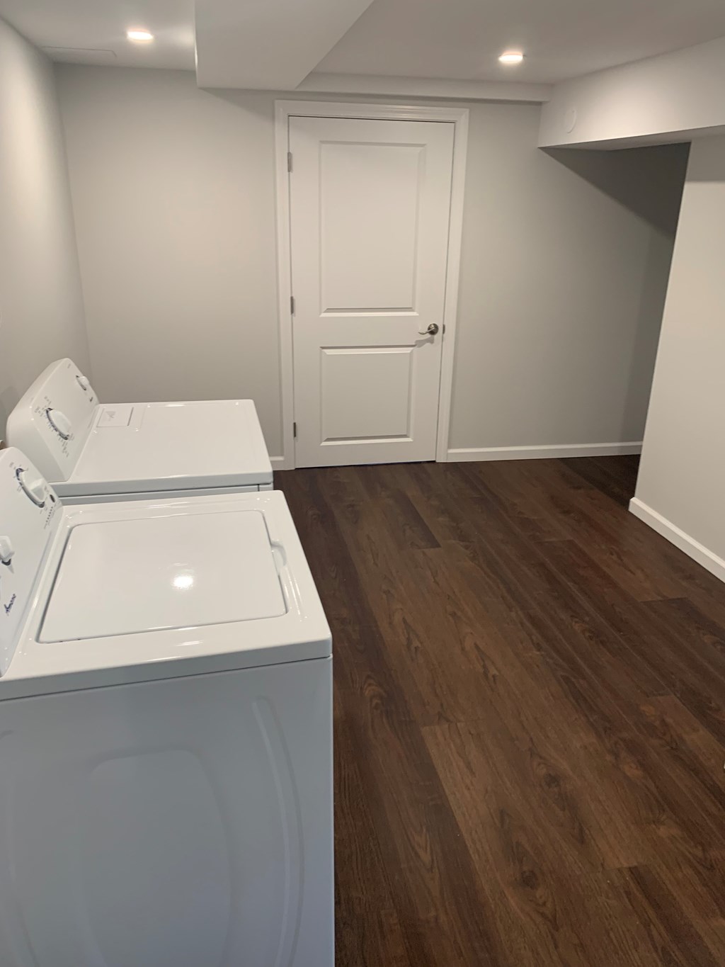 A white washing machine in a room with wood flooring and a white door.