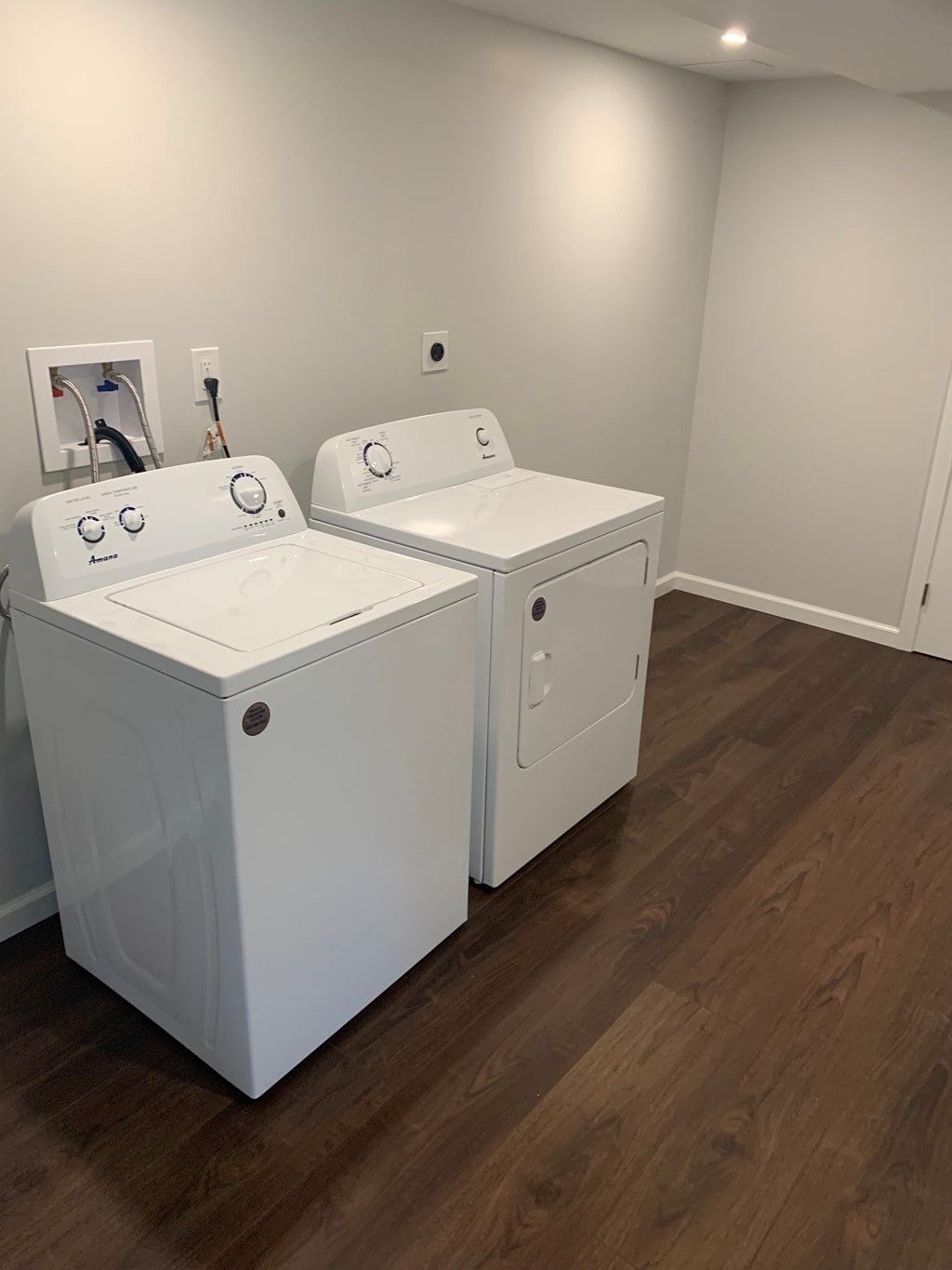 Two white washing machines in a room with wooden flooring.
