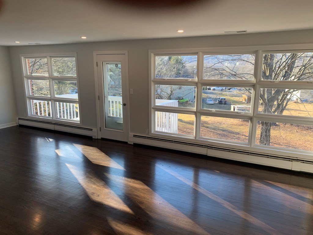 A room with a wooden floor and a view of a tree through the windows.