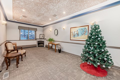 A Christmas tree is in a living room with a chair and a picture.