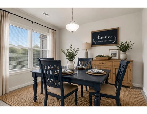 A dining room with a table set for two and a sign that says "home is where we gather".