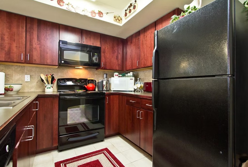 A black refrigerator is in the corner of a kitchen with wooden cabinets.