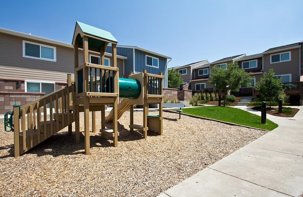 A playground in a residential area with a wooden slide and a green roof.