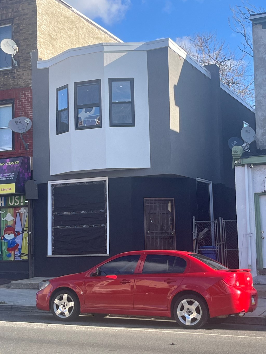 A red car is parked in front of a black and white building.