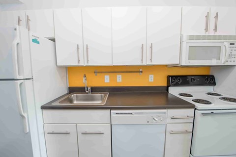 A kitchen with white cabinets and a yellow wall.