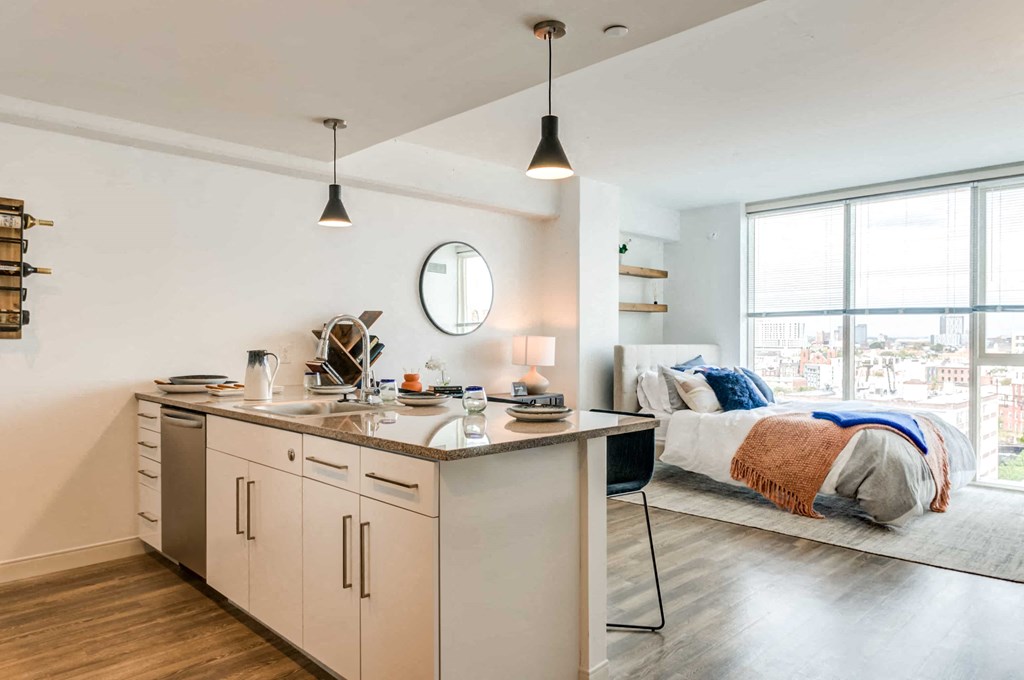 A modern kitchen with a large island and a bedroom with a large window in the background.