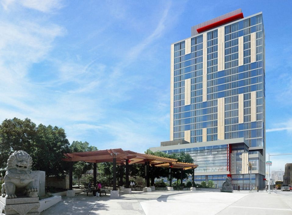 A modern building with a red stripe on the top floor is surrounded by trees and a stone lion statue.