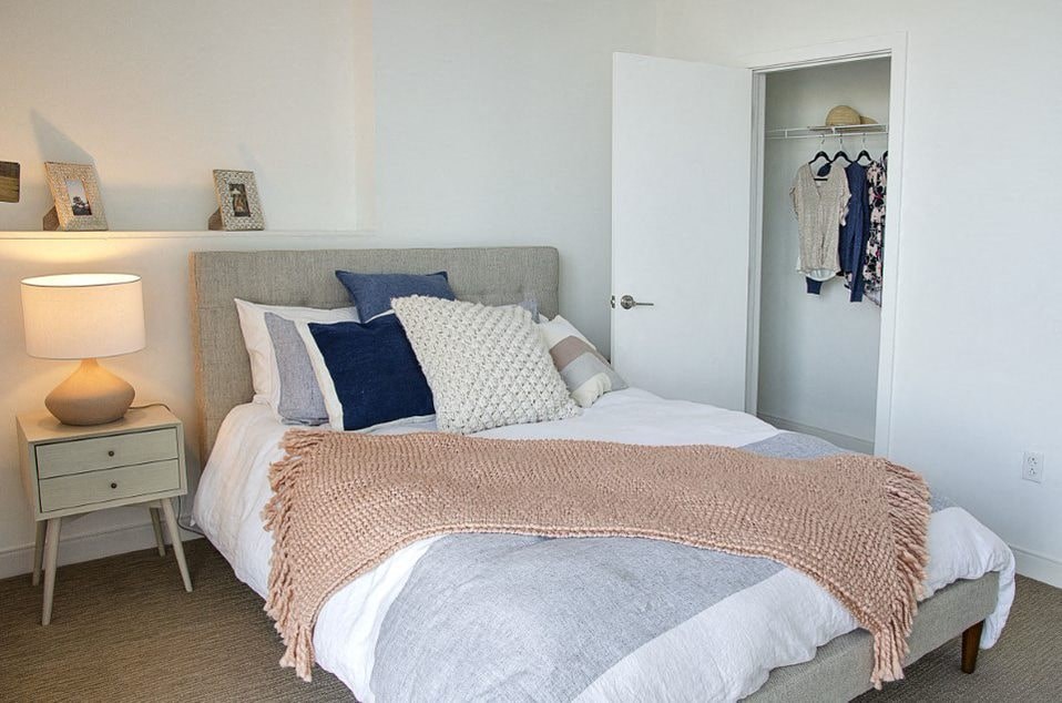 A bedroom with a bed covered in a pink blanket and a white nightstand with a lamp.