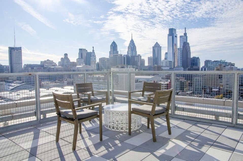 Two chairs and a table on a balcony overlooking a city skyline.