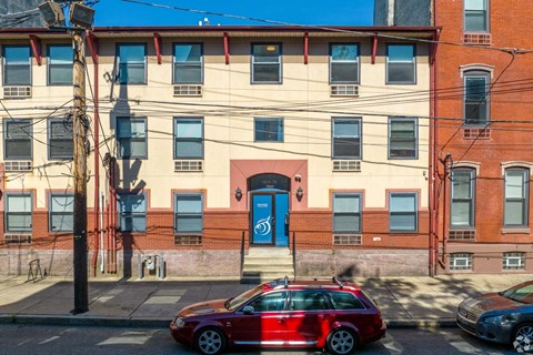 A red car is parked on the side of a street in front of a building with a blue door.