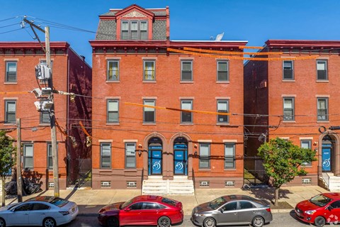 A red brick building with a blue door and a red car parked in front.