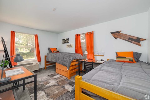 A bedroom with two beds, one with orange bedding, and a wooden headboard.
