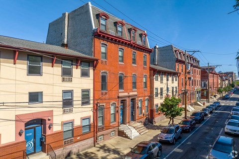 A row of red brick buildings with cars parked on the street.