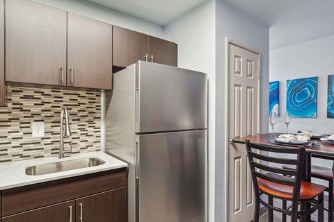 A kitchen with a stainless steel refrigerator and a sink with a brown cabinet.