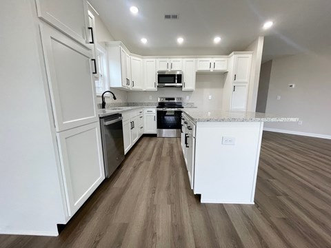 A kitchen with white cabinets and a wooden floor.