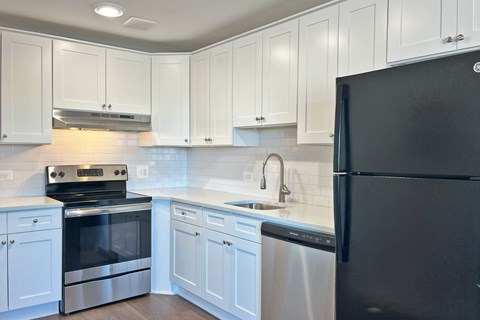 A black refrigerator is in the corner of a kitchen with white cabinets.