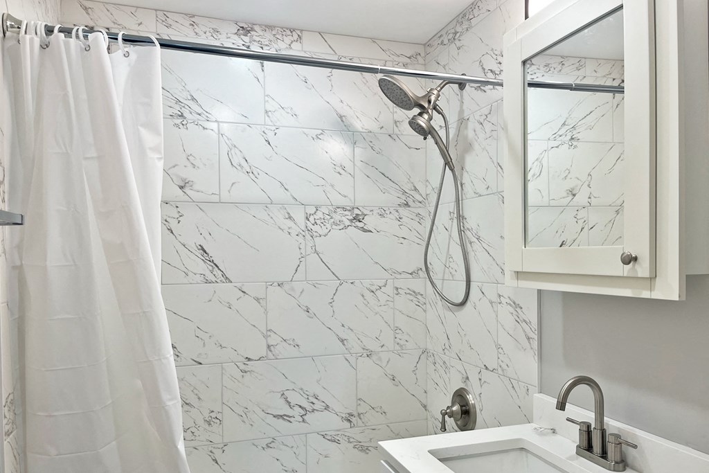 A white shower curtain hangs over a marble shower wall.