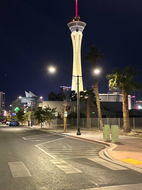 A tall tower with a red spire stands in the night sky above a city street.