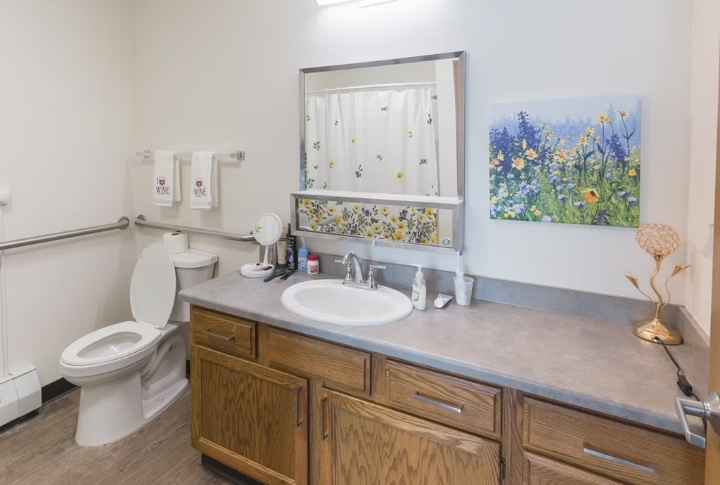 A bathroom with a toilet, sink, and a painting of flowers on the wall.