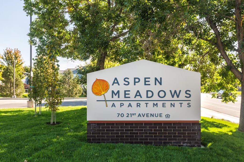 A sign for Aspen Meadows Apartments is shown in front of a tree.