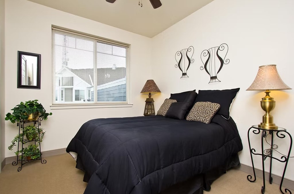 A bedroom with a bed, two lamps, and a plant.