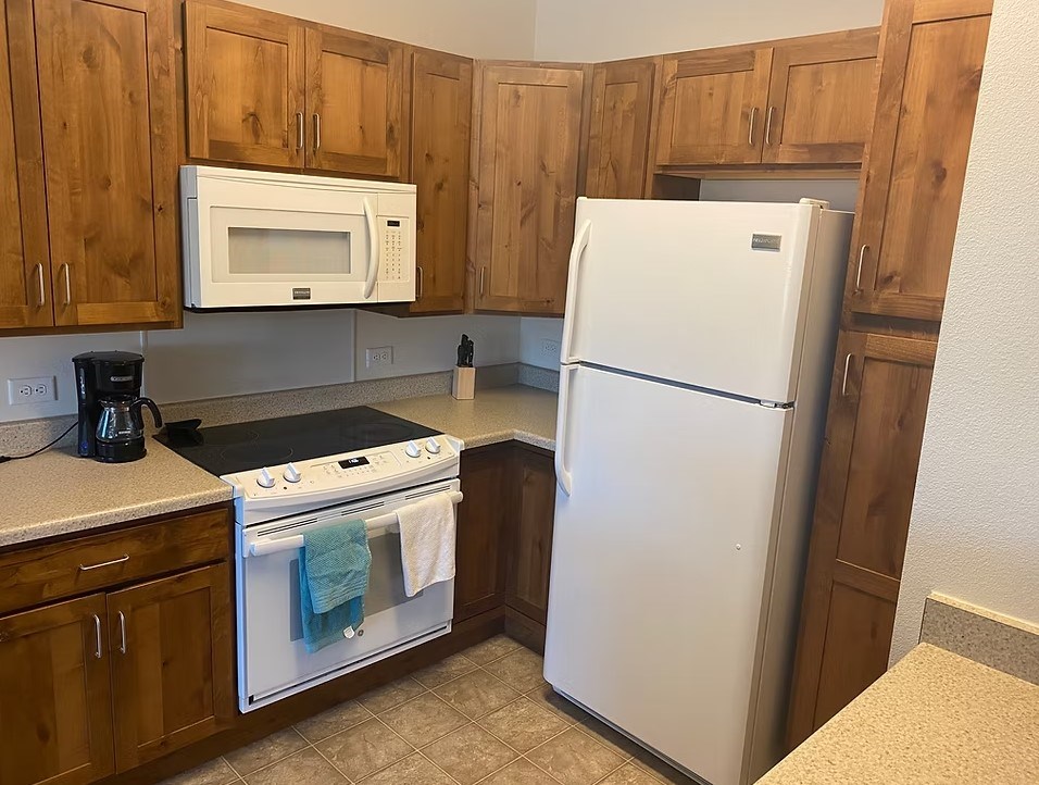 A white refrigerator is in a kitchen with wooden cabinets.