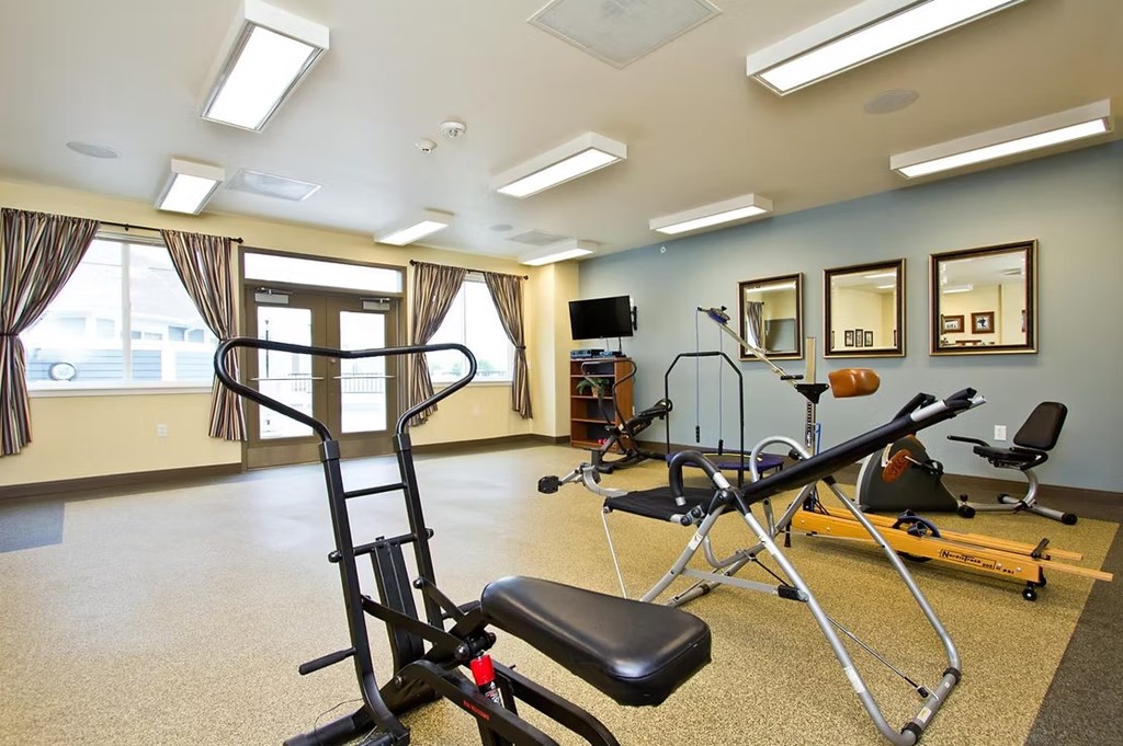A gym room with a rowing machine, a bench, and mirrors on the wall.
