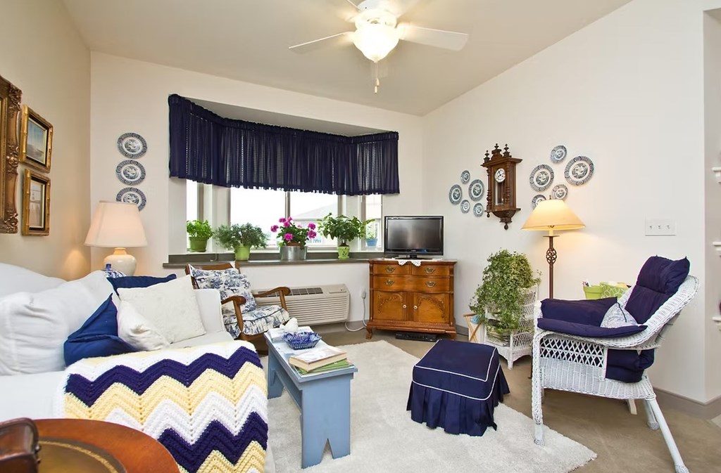 A living room with a white couch, a blue ottoman, a white chair, and a wooden table.