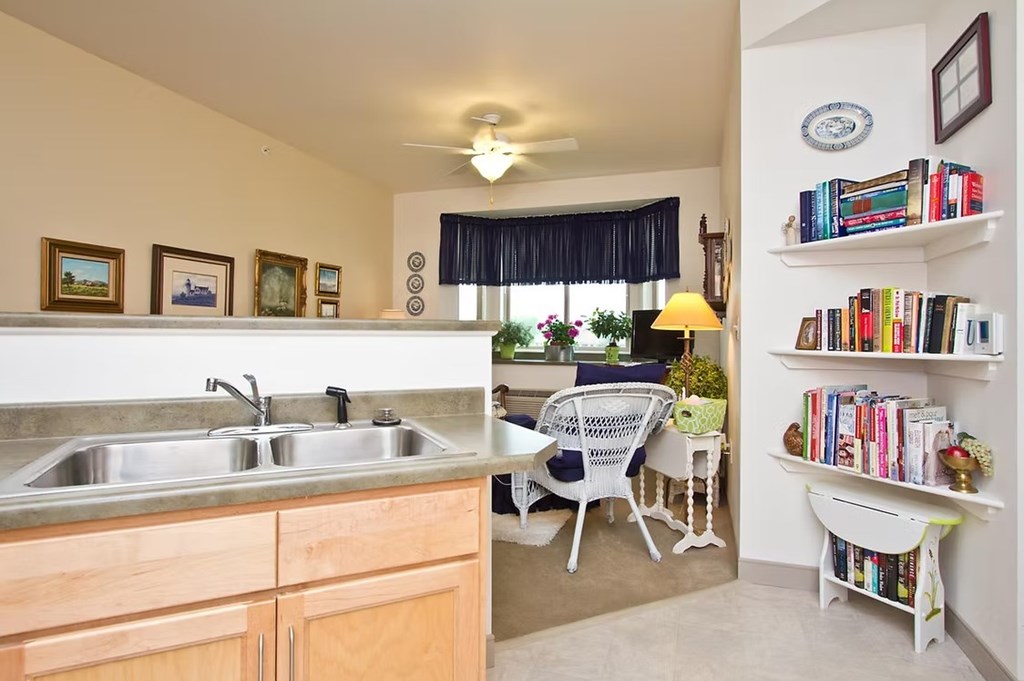 A kitchen with a sink, a chair, and a bookshelf.