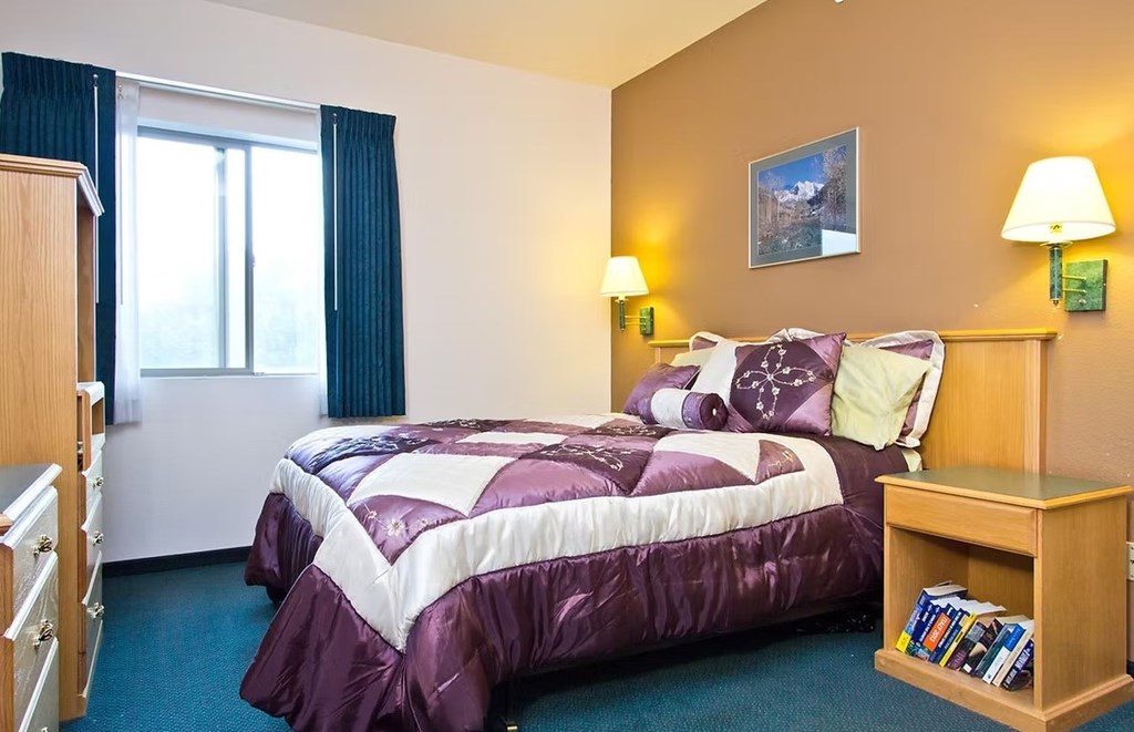 A bedroom with a bed, nightstand, and window.