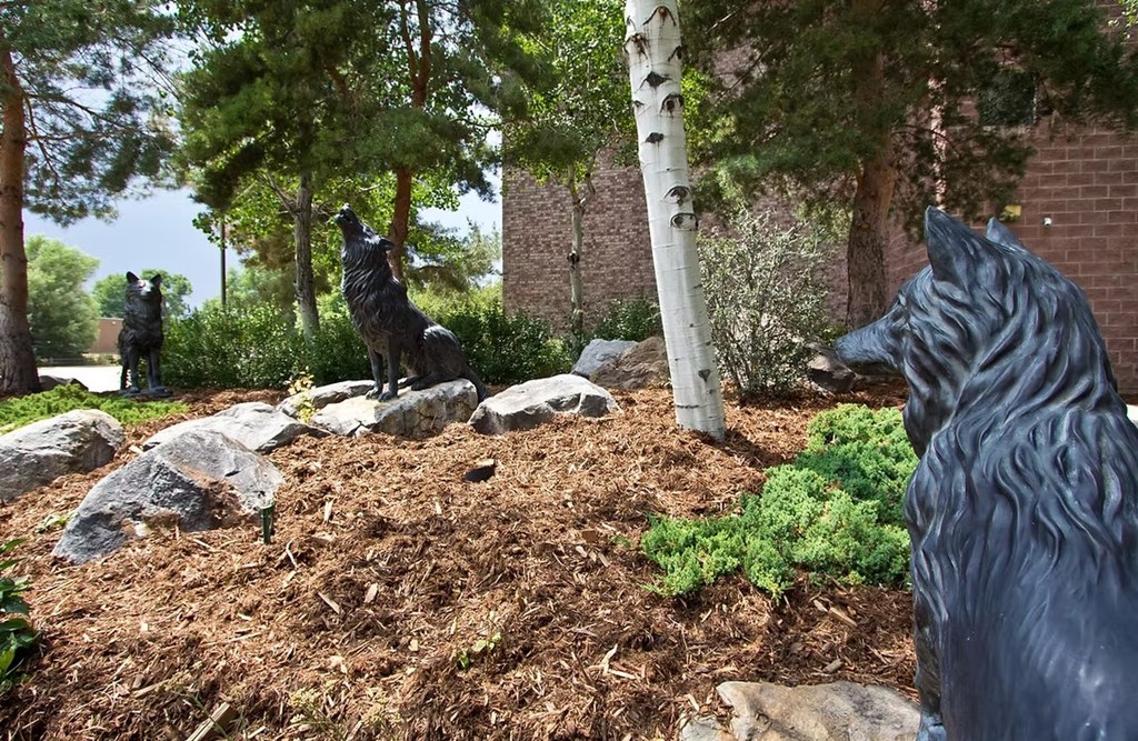 A wolf statue is in the foreground of a garden with other animal statues in the background.