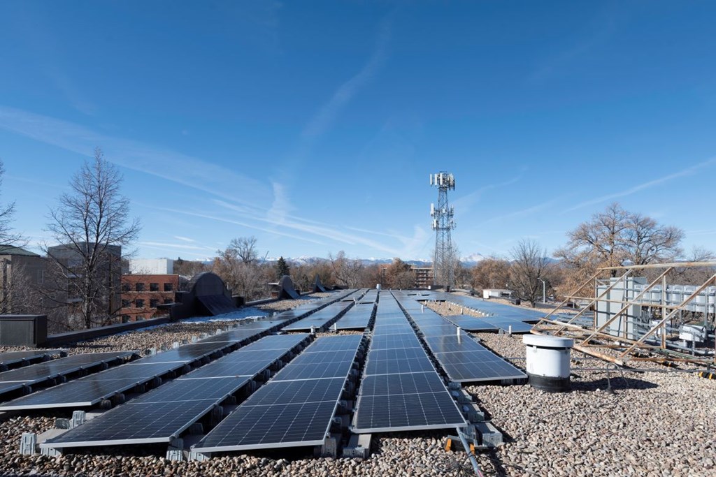 A large array of solar panels is installed on a gravel surface.