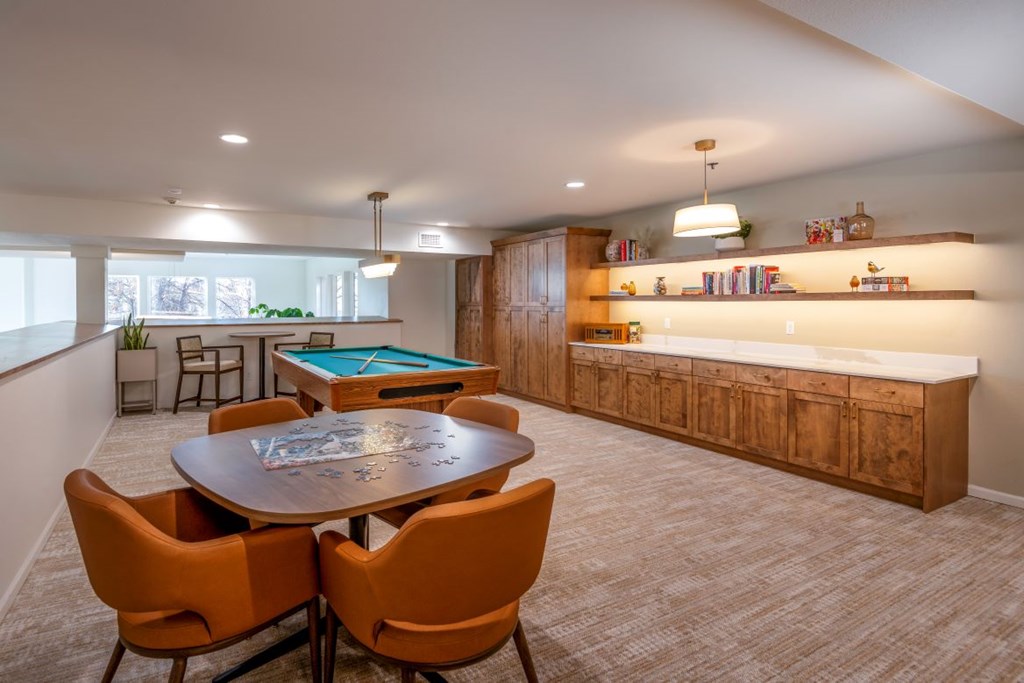 A room with a pool table and orange chairs.