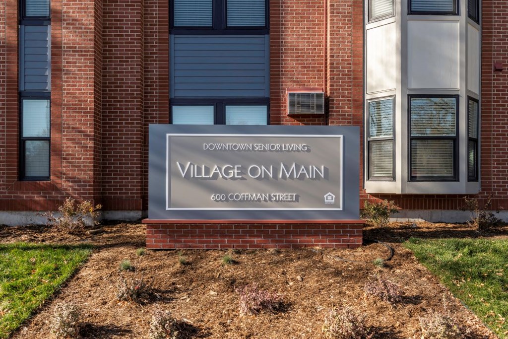 A sign for Village on Main is in front of a brick building.