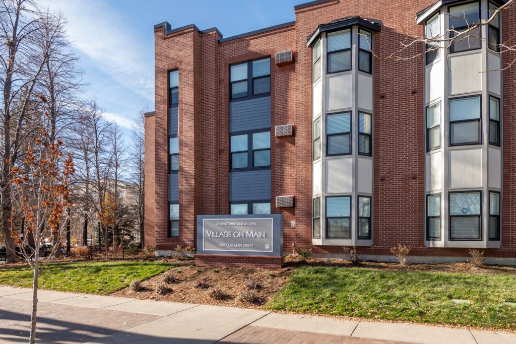 A brick building with the words "Village on Main" on a sign in front of it.