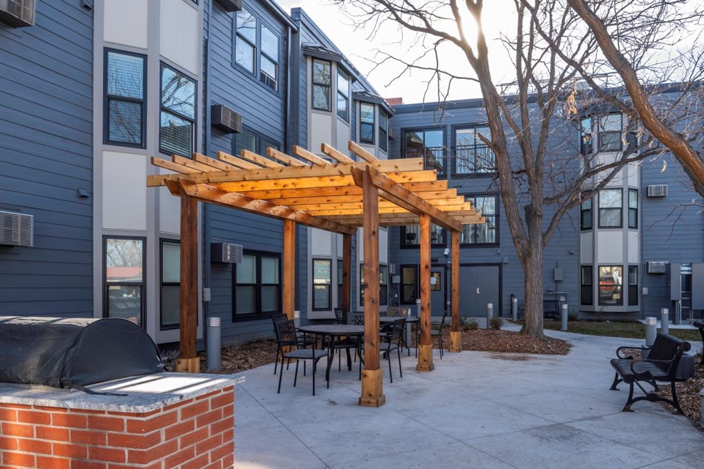 A wooden pergola is in front of a building with a patio.