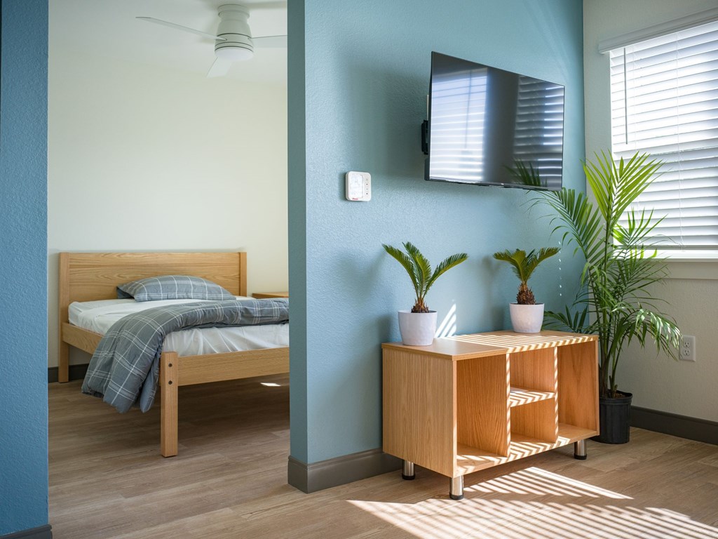 A bedroom with a bed, a nightstand, and a plant.
