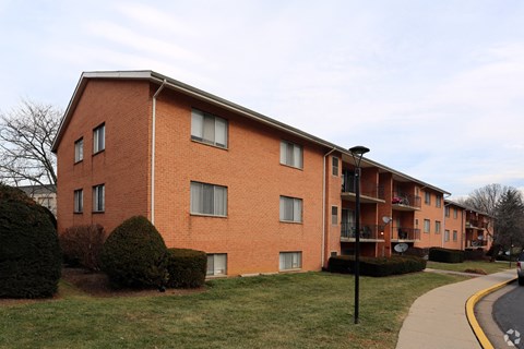 A red brick apartment building with a sidewalk and green bushes.