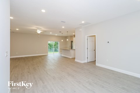 A spacious room with light wood flooring and white walls, with a door on the right and a window on the left.