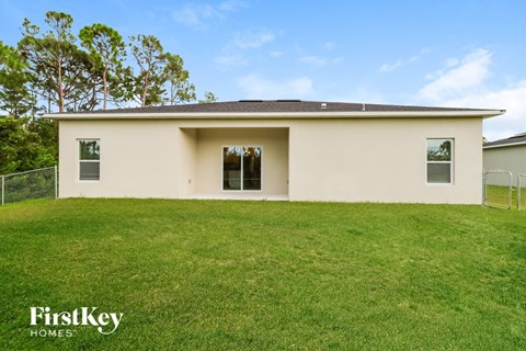 A house with a white exterior and a brown roof is surrounded by a grassy lawn.