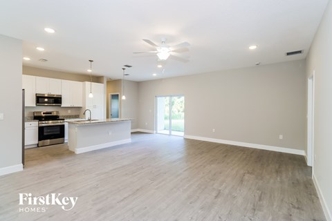 A spacious living room with a kitchen in the background and a sliding glass door leading to a balcony.