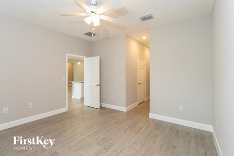 A spacious room with a ceiling fan and light fixture, and a doorway leading to another room.