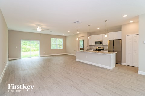 A spacious kitchen with a refrigerator, microwave, and oven, with a dining table and chairs in the background.