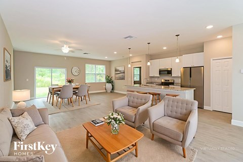 A well-lit, spacious living room with a dining area and kitchen in the background.