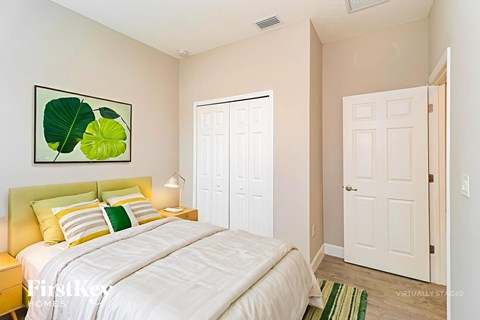 A bedroom with a white bed and a painting of green leaves on the wall.