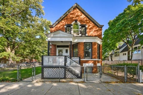 A red brick house with a black and white fence in front.