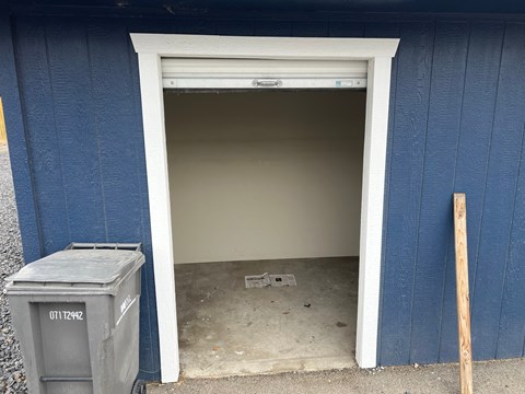 A blue building with a white door and a grey dumpster with the number 0171242 on it.