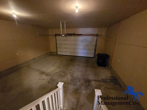 A spacious garage with a white railing and a black trash bin.